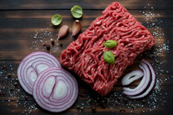Large chunk of Lynch Farms raw ground beef surrounded by fresh herbs, spices and chopped onions