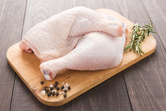 Quartered Lynch Farms raw chicken on cutting board beside fresh herbs and spices