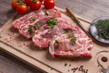 Four Lynch Farms raw pork chops on cutting board with tomatoes, parsley and black pepper